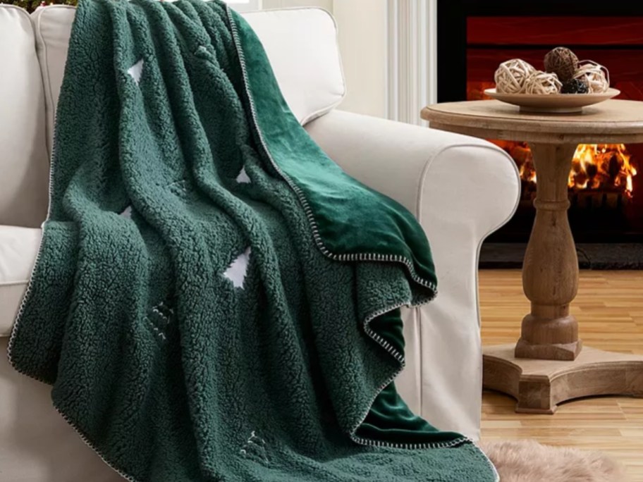 a green plush throw blanket with Christmas trees on it, thrown over a cream color sofa