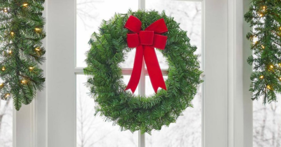 Green Christmas wreath with red bow hanging on window inside home