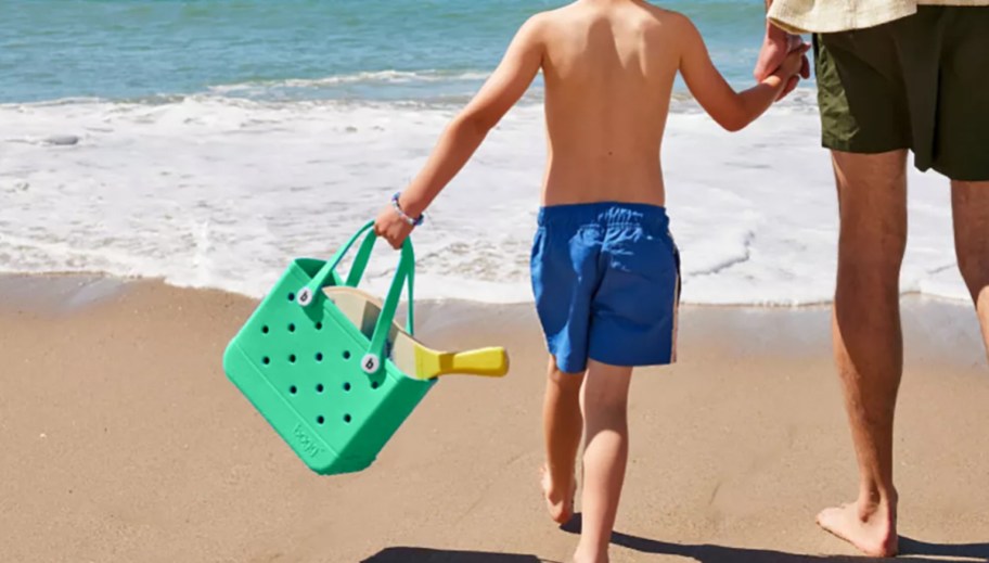 boy carrying a small green bogg bag on beach