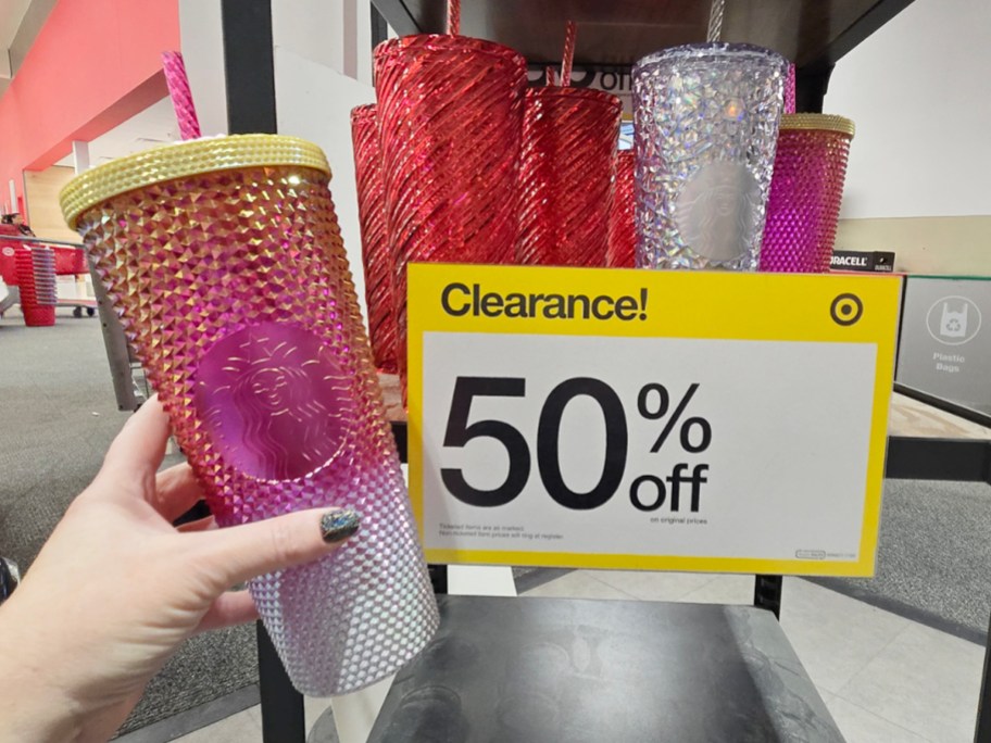 hand holding pink starbucks tumbler near clearance sign 